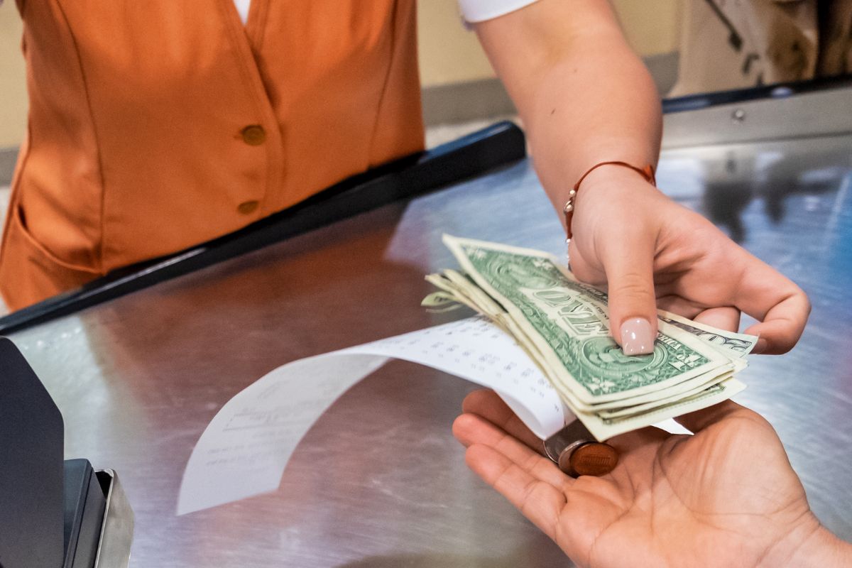 The photo shows a woman's hand paying with cash.