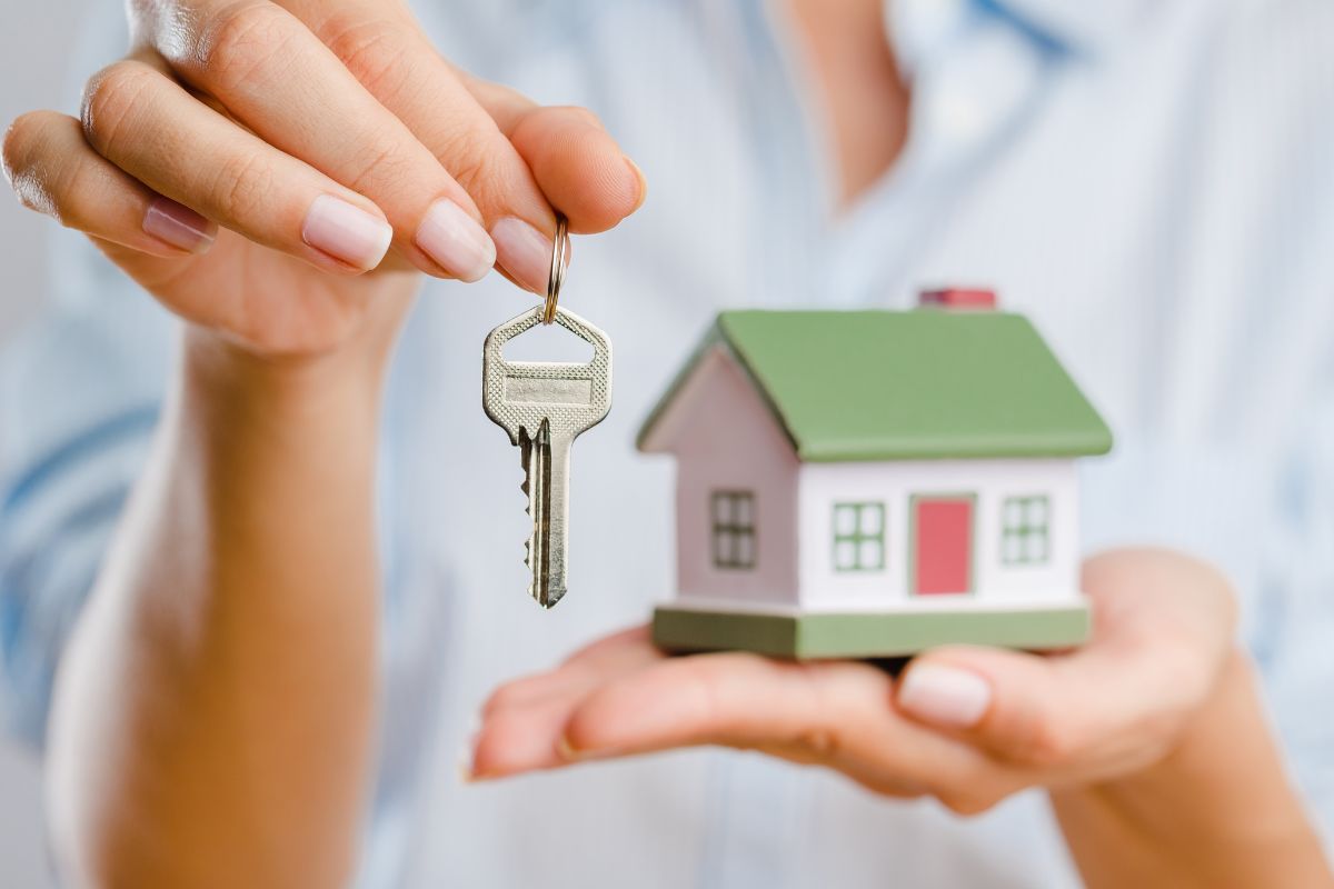 A woman's hand holding a mini house and key.