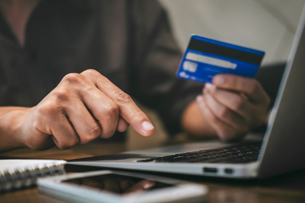 A imagem mostra a mão de um homem pagando com um cartão de crédito.