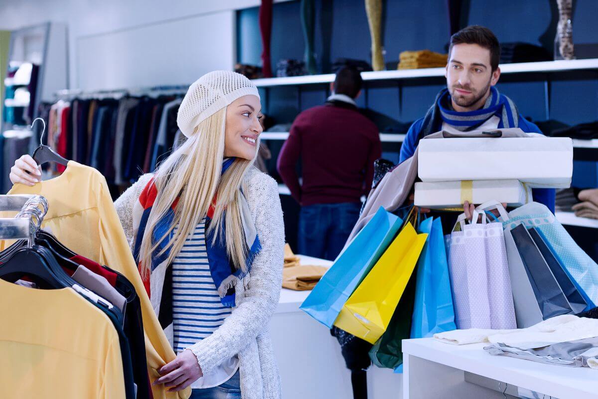 The photo tells about a man carrying shopping bags and a girl picking more items at the store which refers to limiting impulse purchases by implementing a 24-hour waiting rule which helps prioritize needs over wants and save money in the long run.