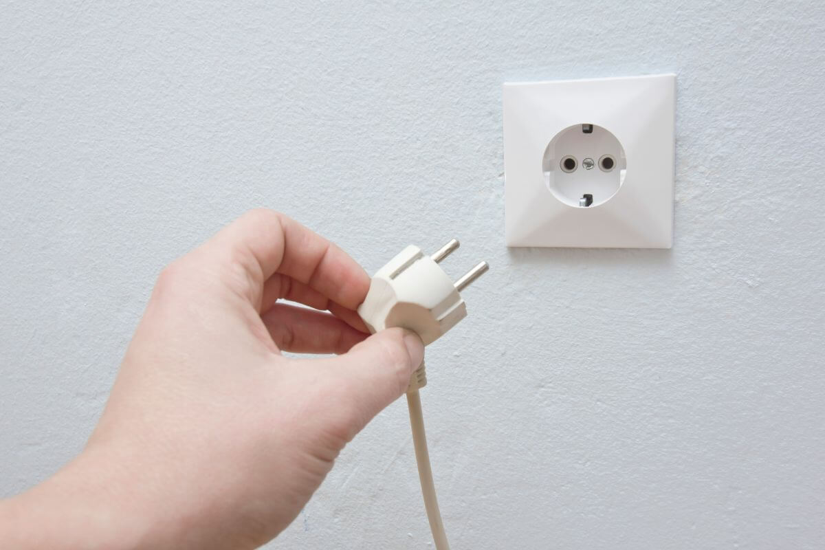The picture of a girl's hand unplugging the power cable out of the outlet means to cut energy costs by reducing electricity use which helps to a big savings over time without much effort.