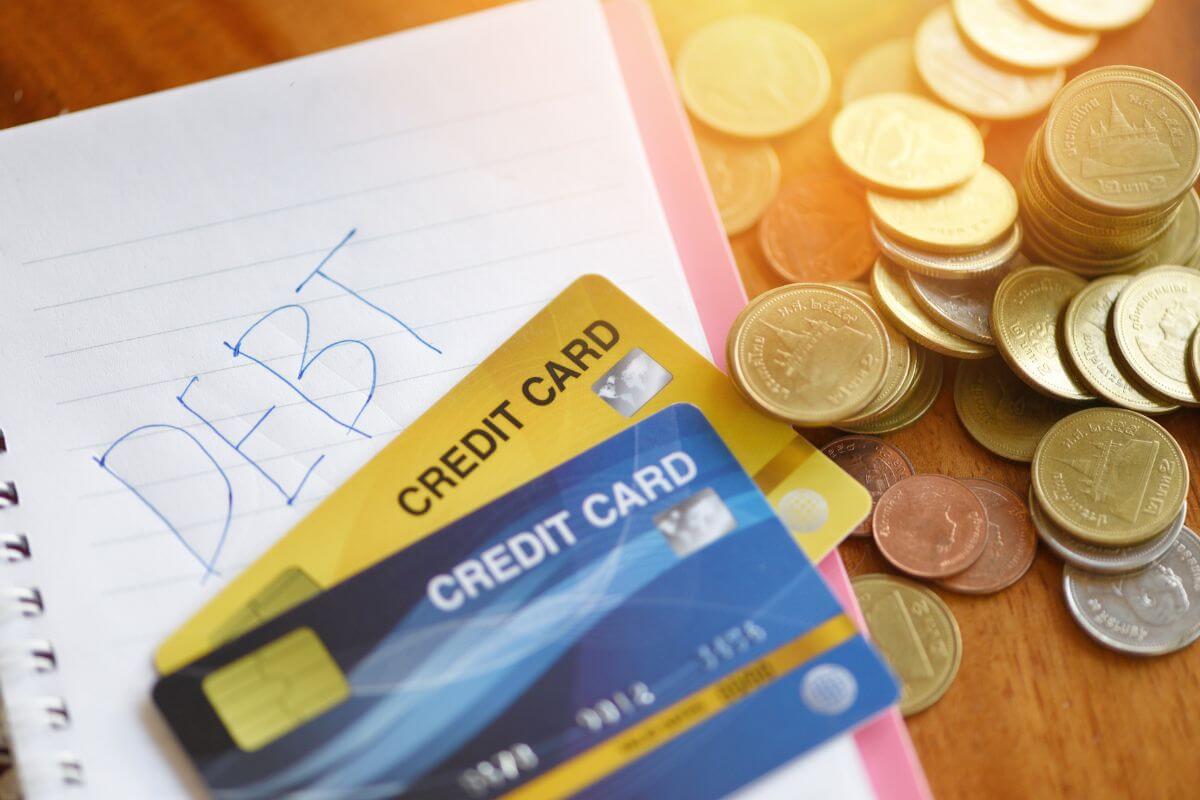 The photo tells about coins, cards, and a notebook with a note that refers to avoiding credit card debt by using cash and sticking to a budget when spending what you have.