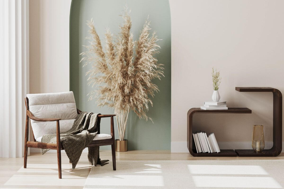 The picture of a living room with a table, a chair, books, and pampas grass represents to practice of minimalist living by reducing unnecessary items and a simple way to free up your budget and focus on your financial priorities.