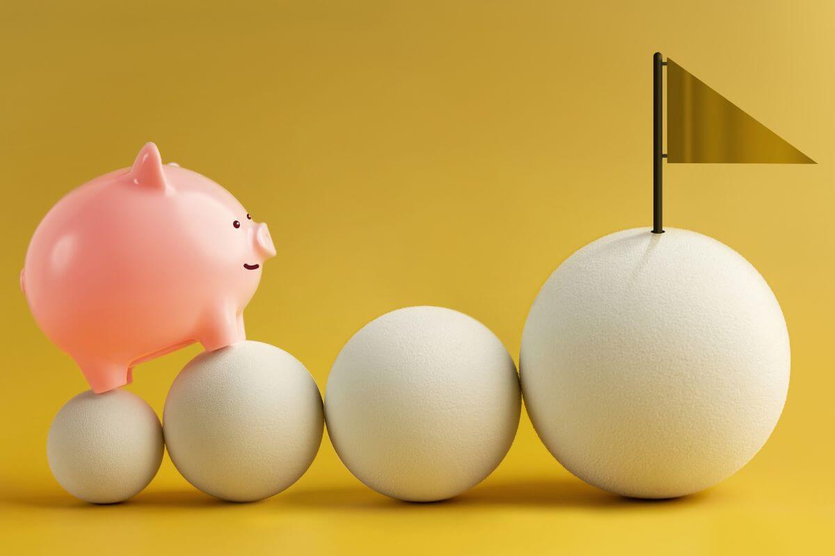 The image shows different sizes of balls with a finish flag and a pink piggy bank indicating to set strict saving goals and prioritize them that help you reach your financial milestone faster.