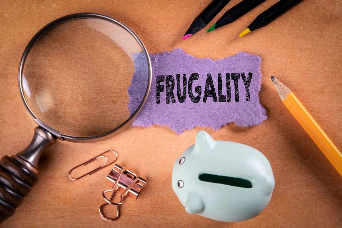 The photo shows colored pens, clips, a magnifying glass, a pen, a piggy bank, and a piece of paper with a note referring to finding over 200 frugal living tips to rock this year and save more money.