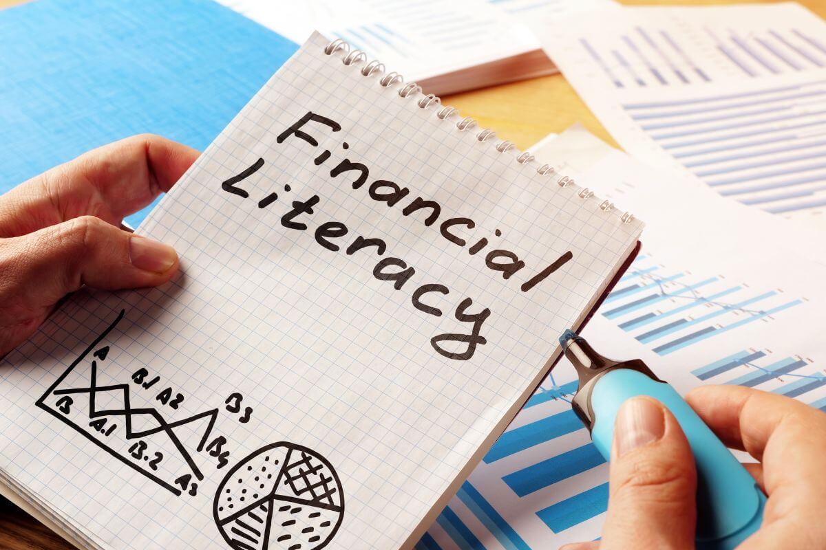 The photo shows papers with graphs and a man's hand holding a marker and a notebook with notes which means to learn a new financial skill to manage your money better, grow your wealth, and feel more confident about your future.