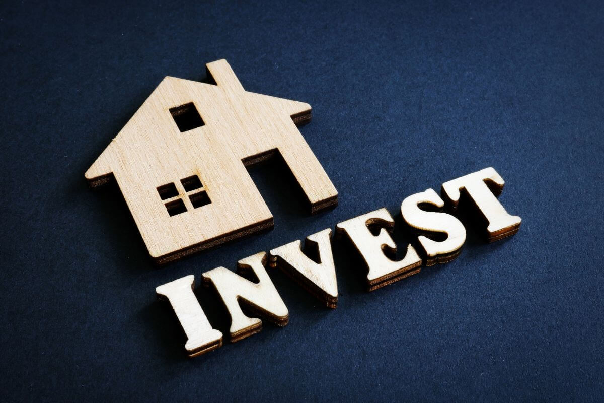 The picture shows a miniature house figure and wooden letters indicating how to invest wisely helps you make better choices and reach your financial goals faster.