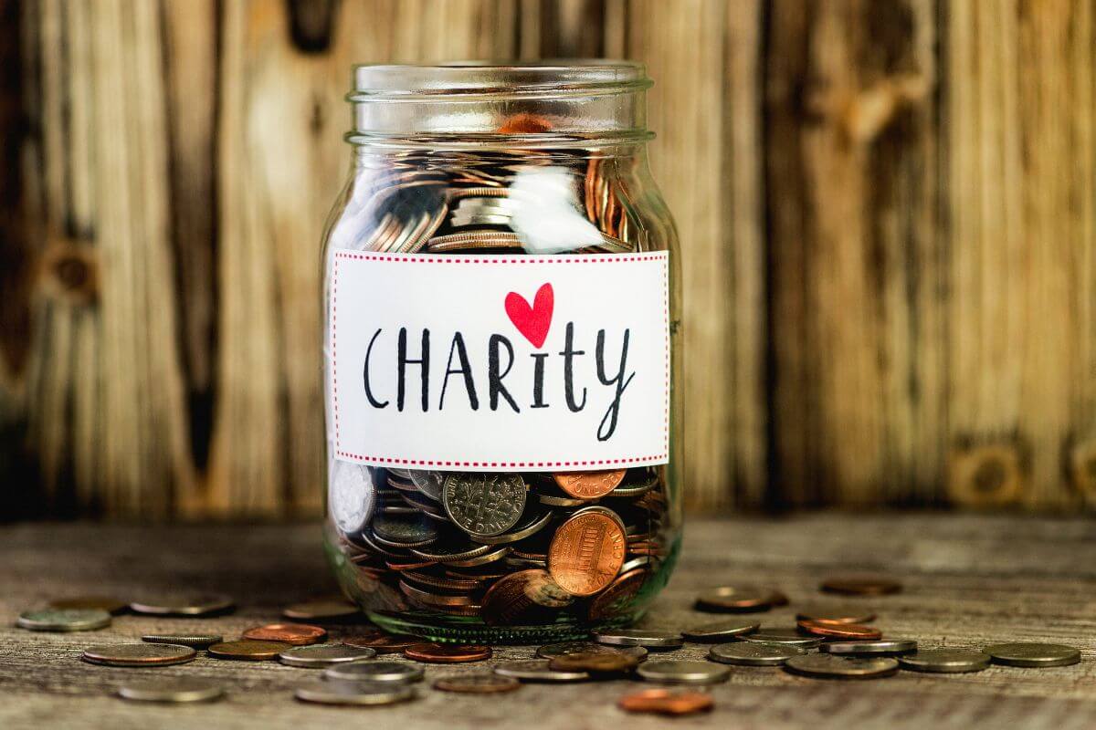 The photo shows coins on the table and a jar filled with coins and with a note which means that increasing your charitable giving to a cause you care about is rewarding and making your finances work for something bigger than yourself.