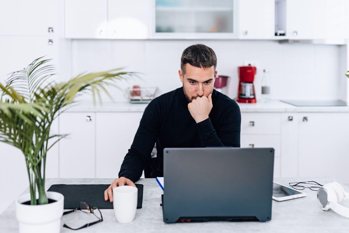 The photo shows a plant, eyeglasses, a headset, a tablet, and a man using a laptop representing to focus on what you can control to feel more in charge of your money.