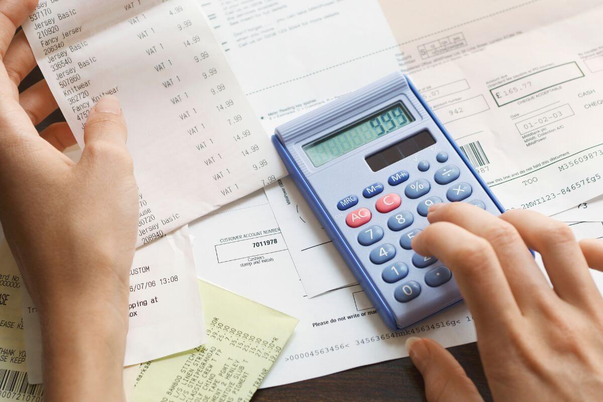 The image tells about papers with contents and a girl's hand using a calculator to compute the receipts which means prioritizing essential expenses first gives you stability and reduces money worries.