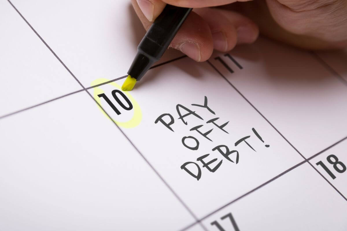 The picture shows a girl's hand encircling the 10th number of a calendar and adding notes indicating how to pay off debt starting small or high-interest to make it manageable and makes progress faster.