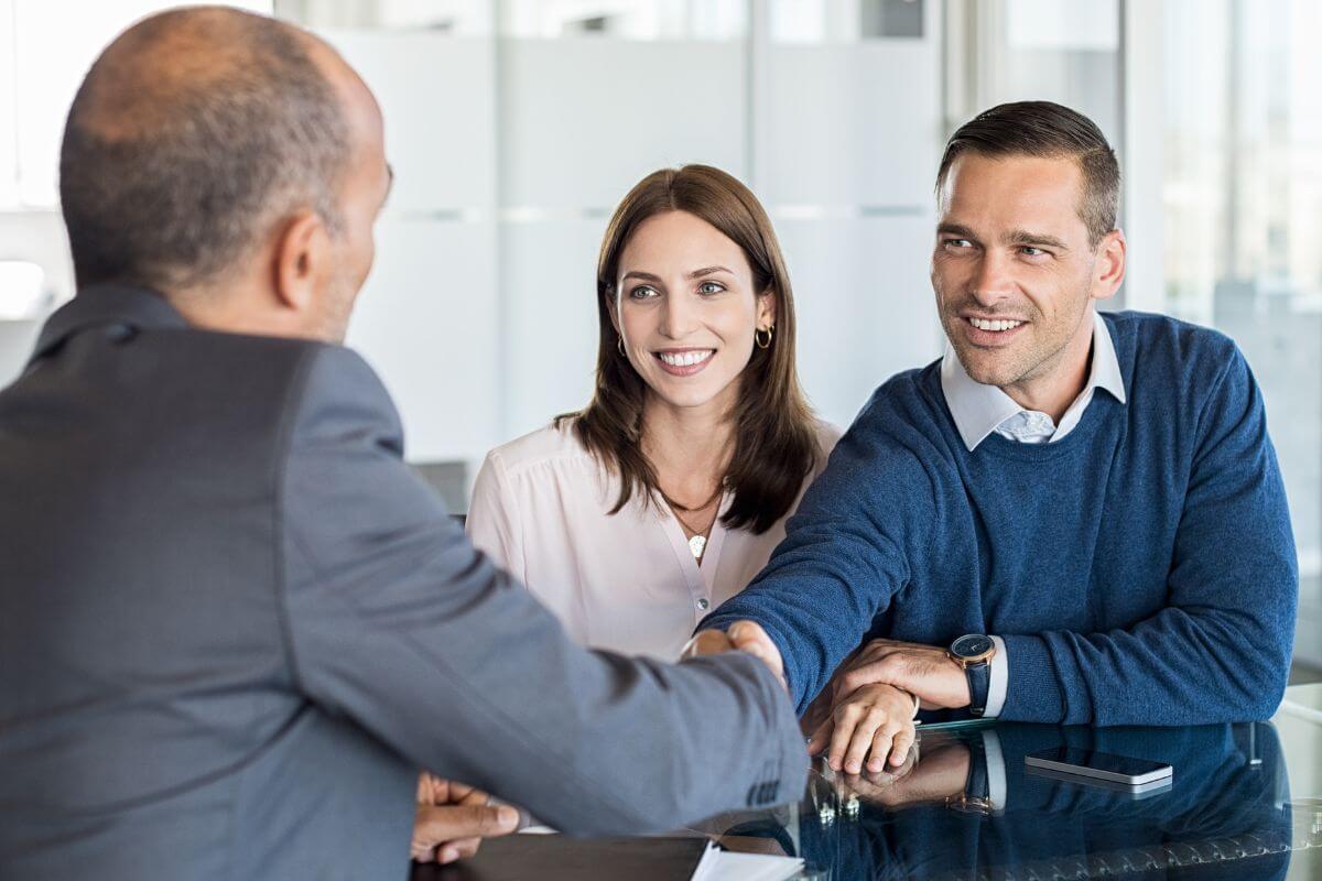 The picture of a couple and a man in a suit hand shaking together which refers to seeking support from a financial advisor helps you make smarter decisions and feel supported in your journey to stability.