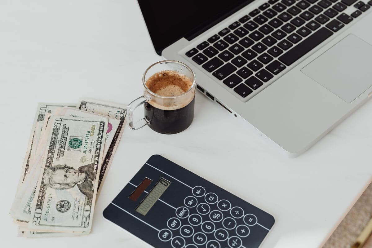 The picture of a laptop, a coffee, a calculator, and dollar bills means using financial tools or apps to organize, track spending, help with the budget, and show where you can save.