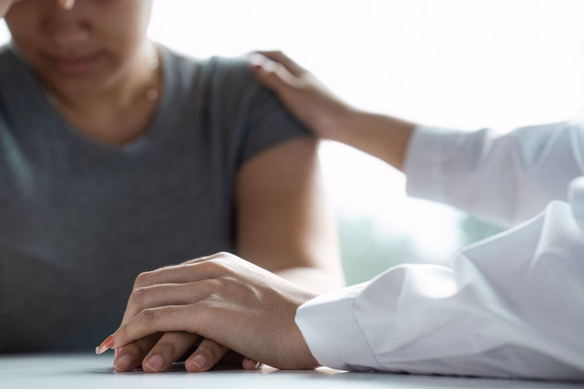 The image shows a girl feeling down and a girl giving a hand and tapping her which means to seek emotional support if anxiety persists can help you process your emotions and focus on finding solutions without feeling overwhelmed.