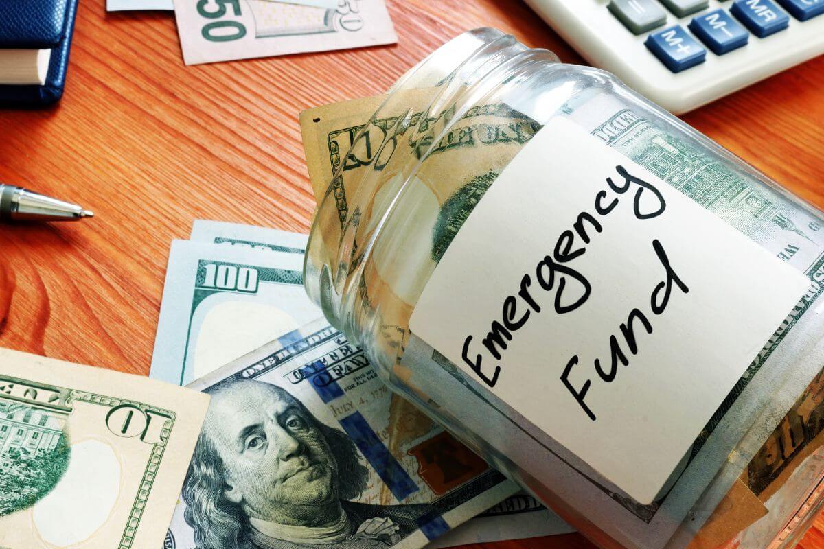 The picture shows dollar bills, a notebook, a pen, a calculator, and a jar with dollar bills and notes which refers to having an emergency fund for unexpected costs that gives you peace of mind.