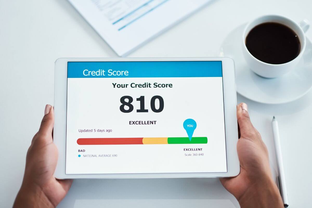 The photo of papers on the table, a coffee, and a girl holding a tablet device with a screen display representing a credit score in a healthy range opens doors to lower interest rates and better financial opportunities.