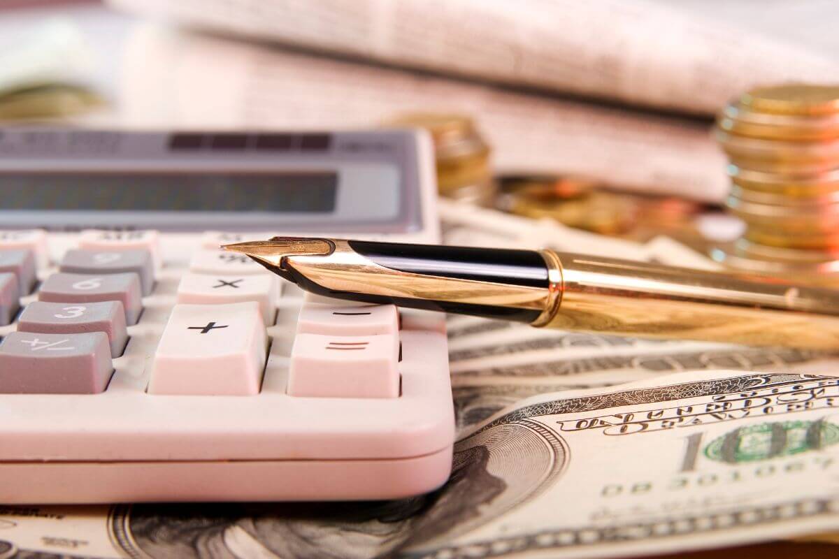 The image of a calculator, coin stocks, a pen, and a dollar bill which refers to a budget by weekly spending limits are easier to stick to than a monthly budget.