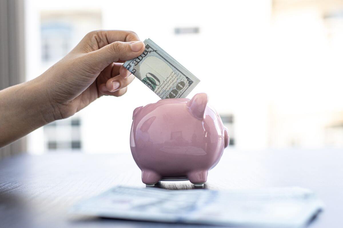 The picture tells about dollar bills on the table and a girl's hand dropping a dollar bill on the piggy bank which means paying yourself first ensures you save before spending.