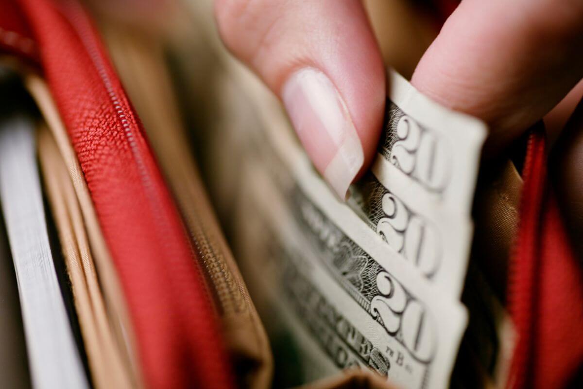 The photo shows a girl's hand pulling out dollar bills from her wallet to set spending caps for a practical and easier to stick with.