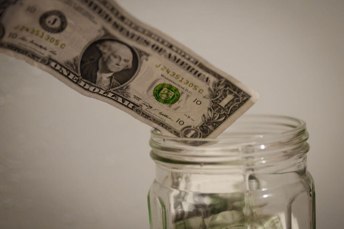 The image shows a dollar bill added to the jar indicating that imposing a fun penalty for overspending keeps you accountable without feeling like punishment.