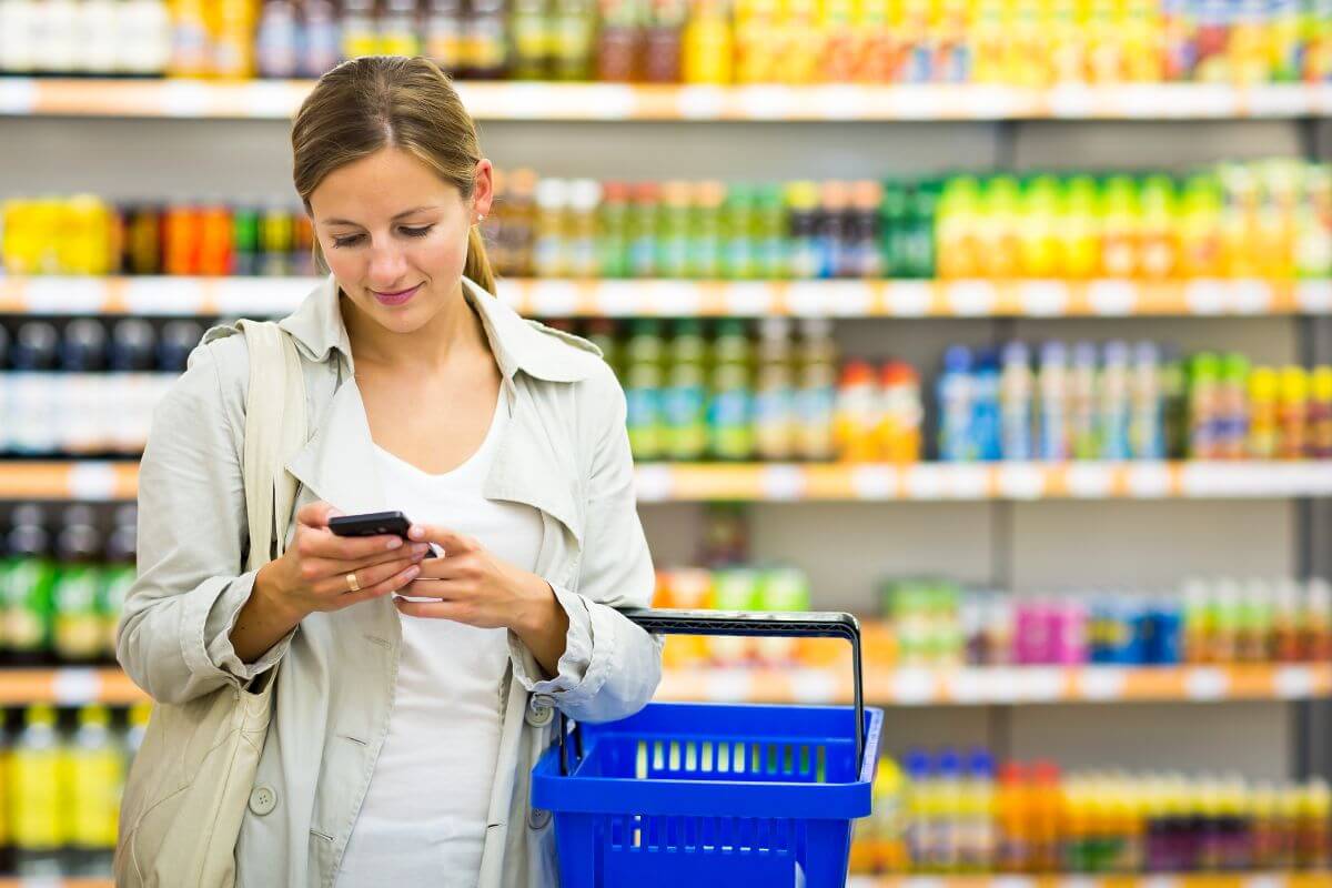 The picture shows product displays and a girl carrying a cart while using a phone which refers to switching to weekly grocery shopping with a strict cash limit that helps you stay disciplined and stick to a set amount.