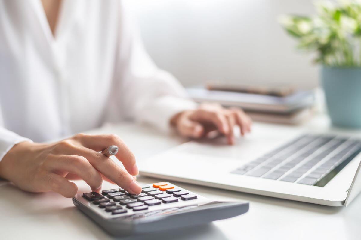 The picture of a plant, notebooks, and a girl using a calculator and a laptop to find more ideas on how to budget better by reaching your financial goals and living stress-free.