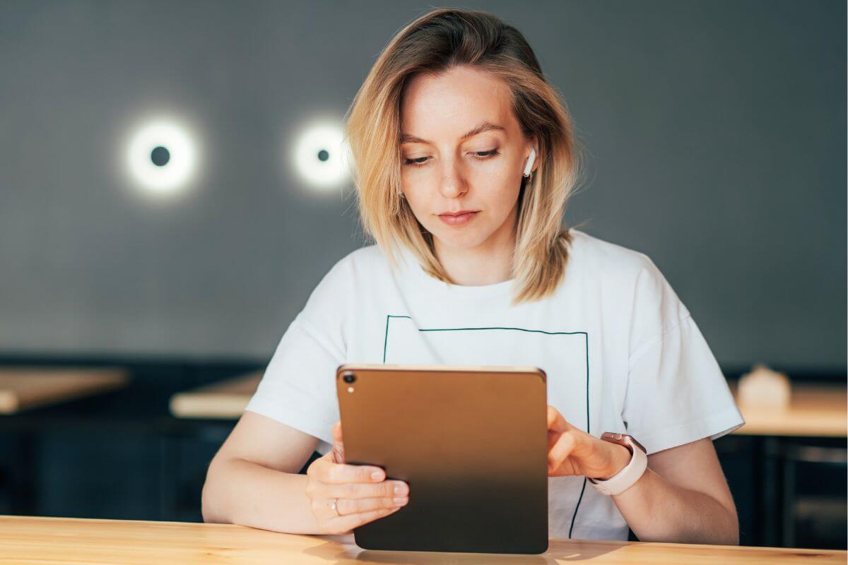The picture of a girl using a tablet device to review and reduce subscription services helps you cut the ones you don't need.