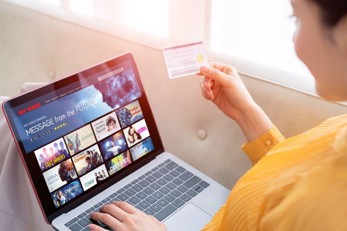 The picture shows a girl using a laptop while holding a card which refers to redirecting subscription savings toward debt helps you focus on getting out of debt.