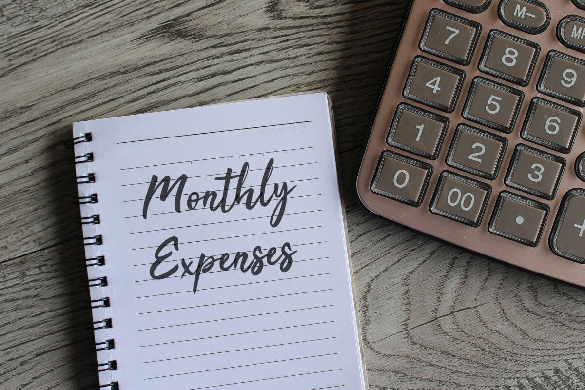 The photo shows a calculator and a notebook with notes indicating to review your monthly expenses and cut non-essentials to help free up money to put toward your retirement account.