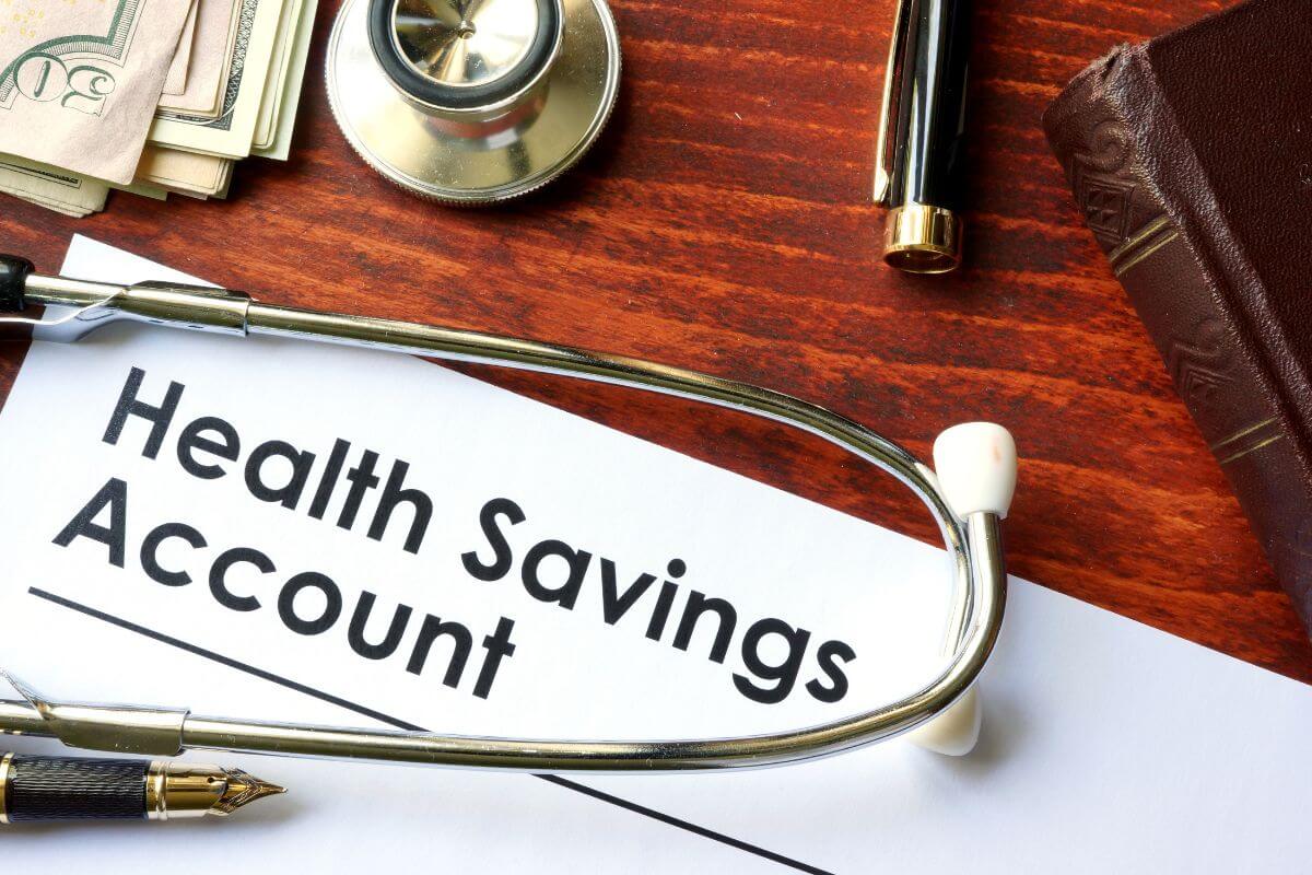 The photo of dollar bills, a pen,  a wallet, a stethoscope, and a piece of paper with notes refers to starting a health savings account for medical expenses while reducing your taxable income.