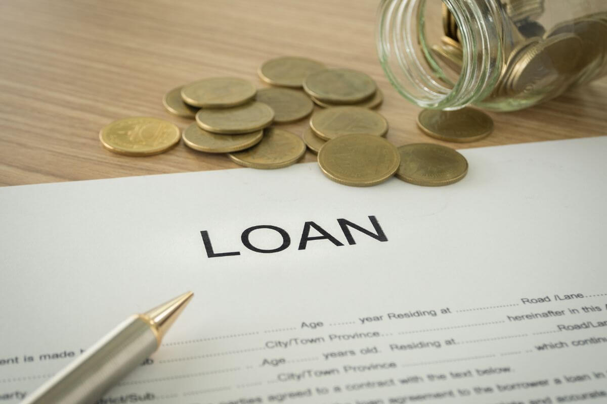The photo tells about a jar filled with coins, a pen, coins on the table, and a piece of paper with notes referring to refinance high-interest loans that can save you hundreds each month.