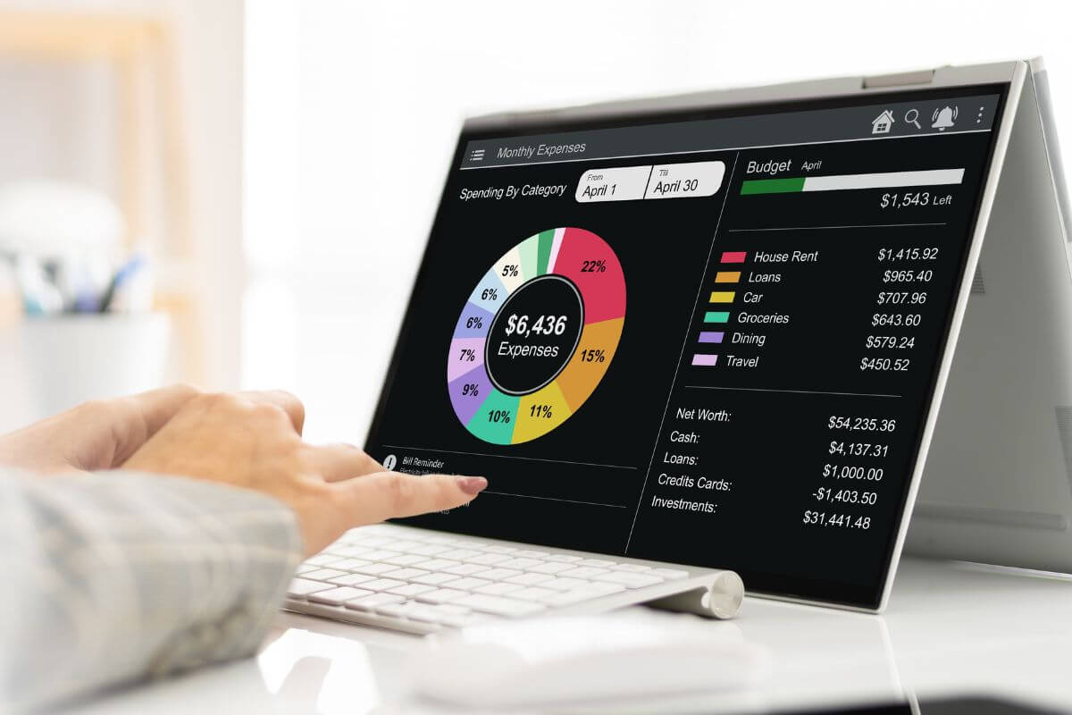 The image shows a girl's hand using a laptop with a screen display which means using budgeting apps that round up your spending and turn spare change into real savings.