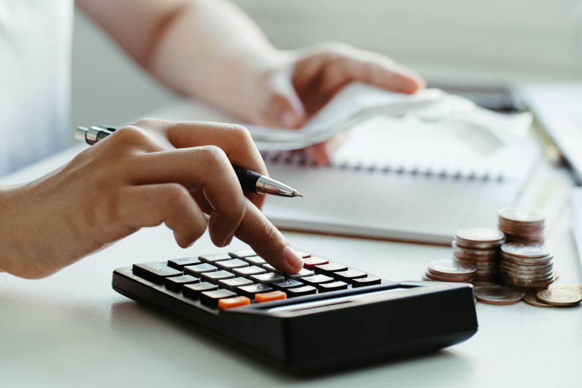 The photo tells about coin stocks, a notebook, and a girl's hand using a calculator while holding a receipt which means to consider a zero-based budget that ensures no money goes to waste while making your goals a priority.