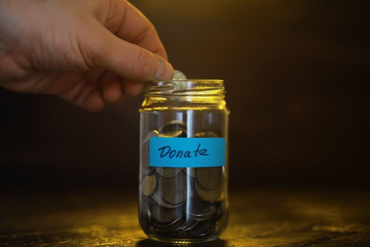 The man's hand placed a coin on the jar filled with coins and with a note referring to automated charitable contributions and helping maximize your tax deductions.