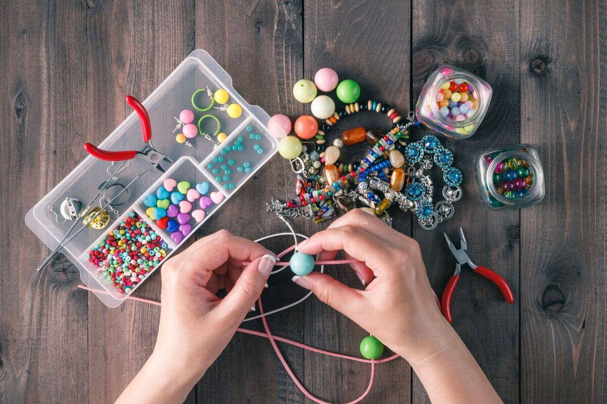The photo of tools and a girl's hand creating custom handmade jewelry to sell online to turn your creativity into income.