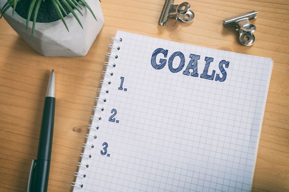 The image tells about clips, a pen, a plant, and a notebook with notes indicating that breaking goals into smaller steps makes them less overwhelming and easier to manage.