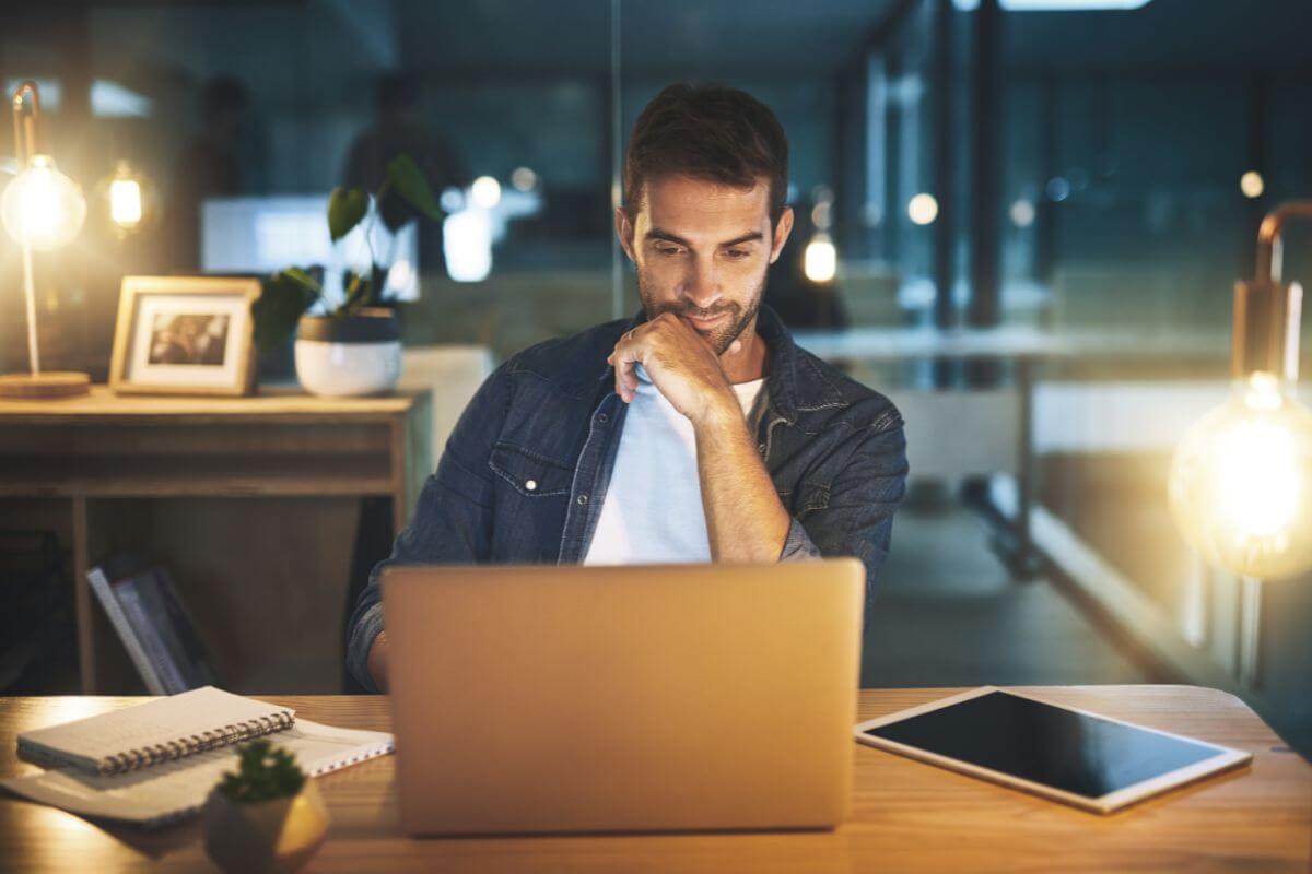The image shows a tablet device, notebooks, and a man using a laptop indicating that focusing on one or two major goals at a time helps you accomplish more and stay motivated to reach the finish line.