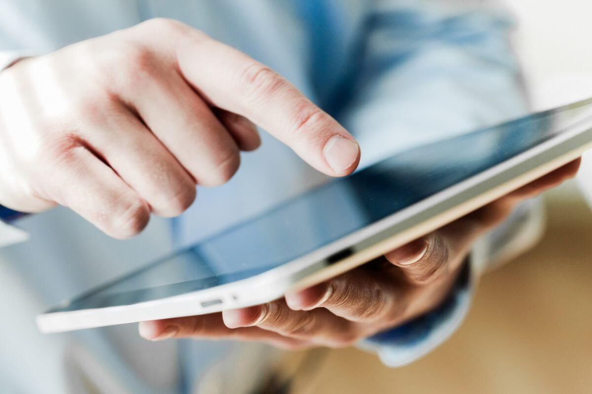 The picture shows a man's hand using a tablet device which means using tools or apps to stay organized and on track helps you manage your progress and keep deadlines in check.