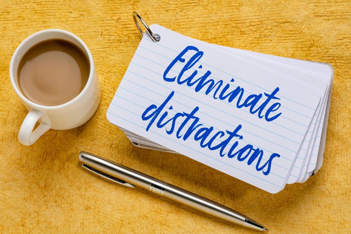 The image tells about a coffee, a pen, and papers with notes referring to eliminating distractions that hinder progress making it easier to stick to your plan and stay on track.