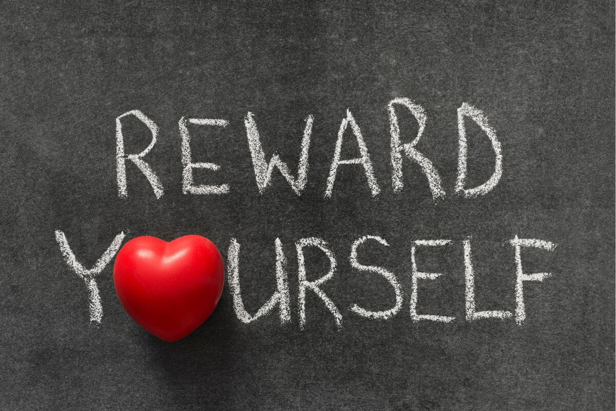 The photo shows a blackboard with mini hearts and notes referring to developing a reward system for reaching milestones makes working toward your goal more enjoyable and helps you stay consistent.