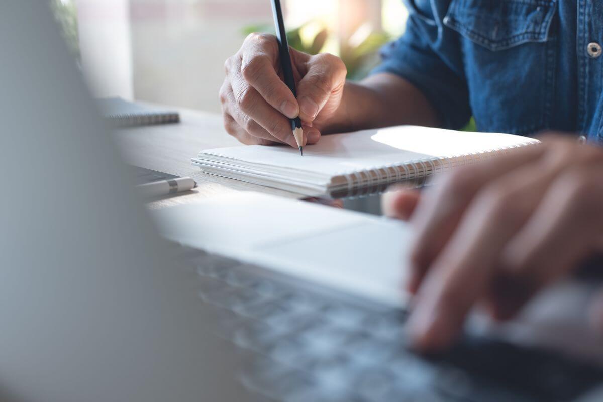 The picture shows a man watching online and writing in a notebook which means continuously learning and adapting strategies helps you find what works best.