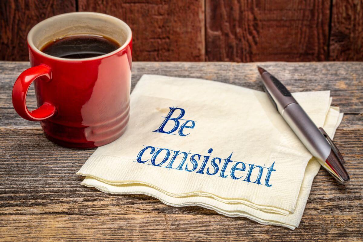 The picture tells about a pen, a coffee, and paper napkins with notes indicating that focusing on consistency over perfection keeps you moving closer to your goals.