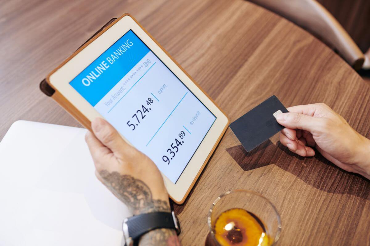 The picture shows a man's hand holding a tablet device and a card indicating to set up automatic savings transfers to grow your savings without needing to think about it every month.