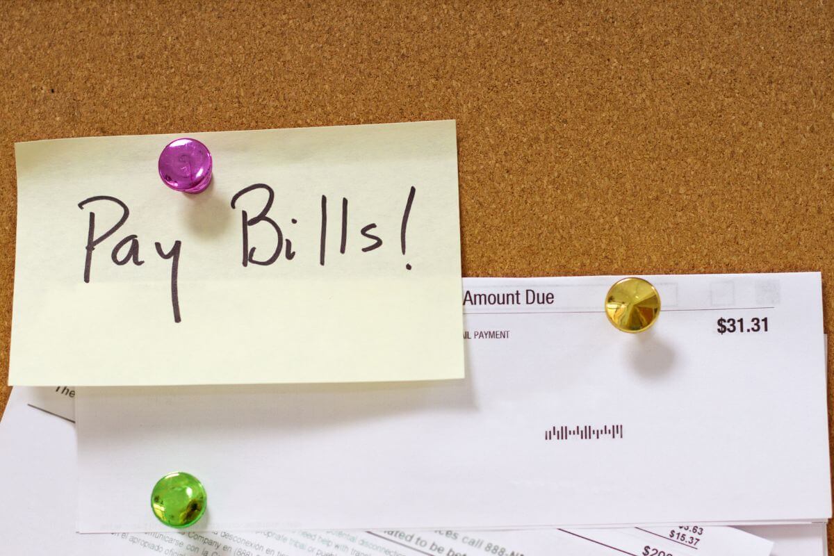 The image shows papers with notes and pins referring to paying bills on time to avoid late fees and protect your credit score. 