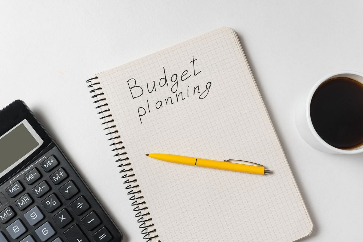 The photo of a coffee, a calculator, a pen, and a notebook with notes refers to creating a budget that works to pay off debt and build a brighter financial future.