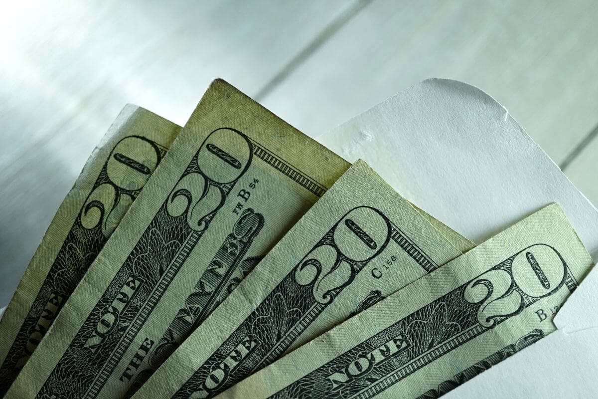 The photo shows an envelope with dollar bills which means using the envelope method for budgeting and setting aside specific envelopes for retirement contributions each month.