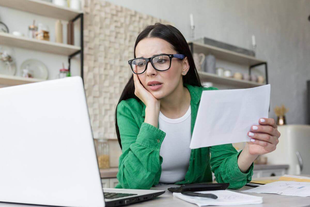 The photo shows papers on the tables, a pen, a calculator, and a girl looking at a laptop while holding a paper refers to considering paying smaller debts first which frees up money to target larger debts as you go.
