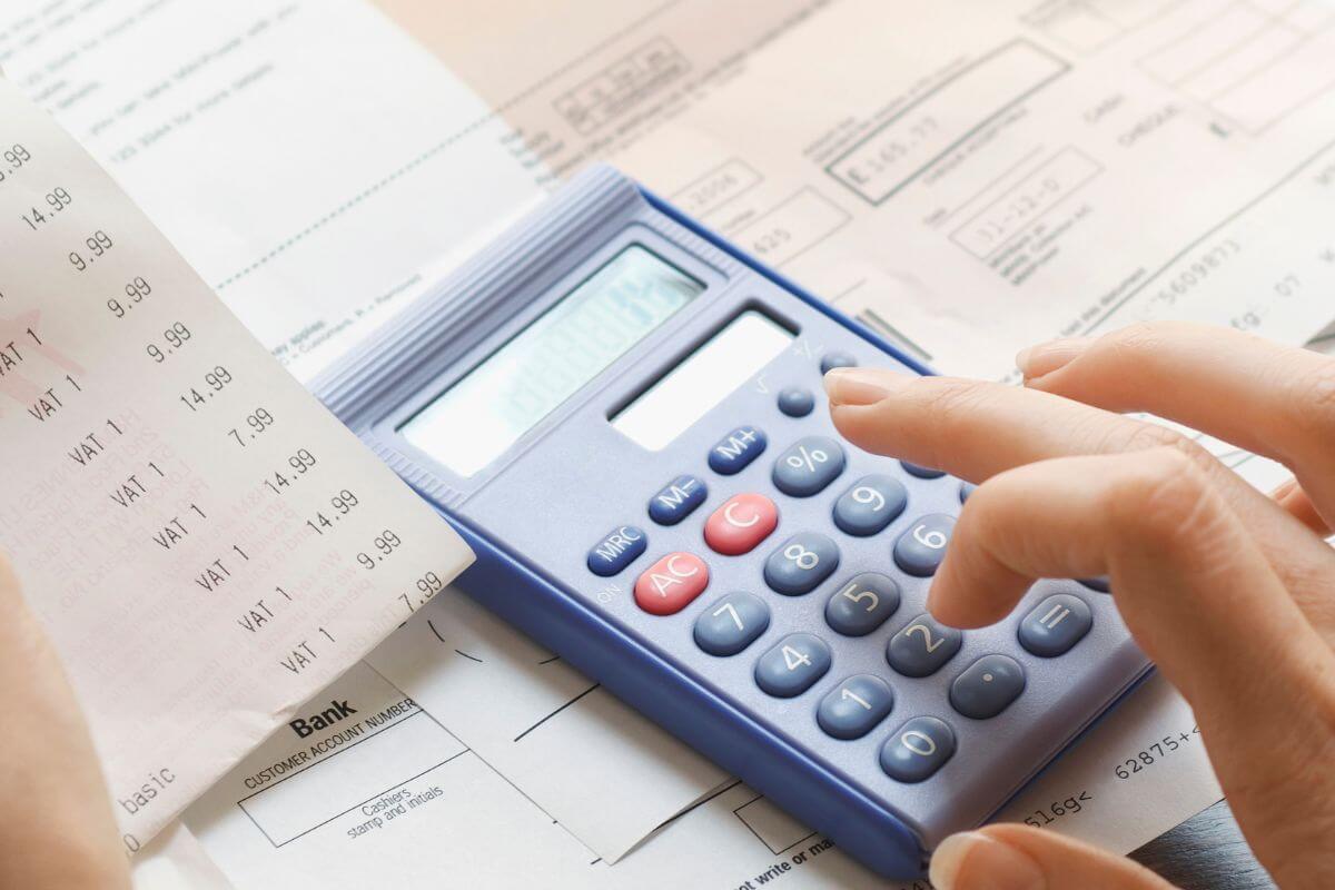The image shows papers with notes and a girl's hand holding a receipt while calculating indicating to track expenses to cut back and redirect that saved money toward your debt.