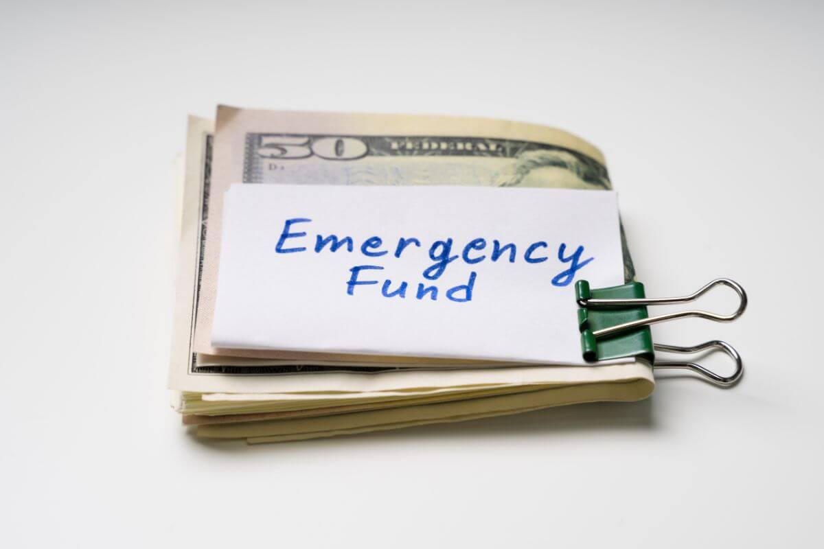 The picture shows dollar bills and a piece of paper with a clip indicating to build an emergency fund to avoid relying on credit cards for unexpected expenses.