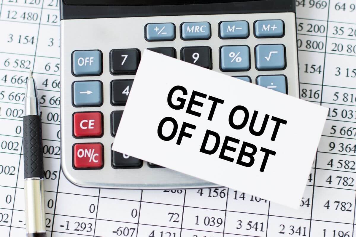 The image shows a pen, a calculator, a piece of paper with numbers behind it, and a piece of paper with notes indicating how to get out of debt today and build a strong financial future.